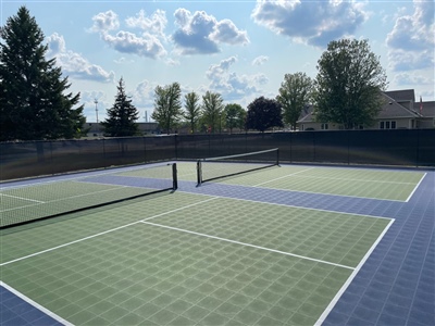 Outdoor sports court with a green and blue surface, white lines, and a tennis net, surrounded by trees and a black fence in Dayton.