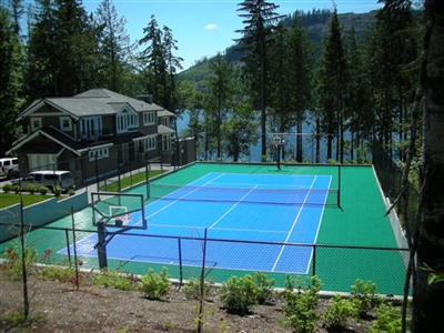 Outdoor residential sports court with a green and blue surface, featuring basketball hoops and a tennis net.