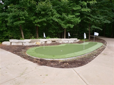 Outdoor putting green with white flags, surrounded by a concrete pathway, mulch, and trees in the background in Excelsior.