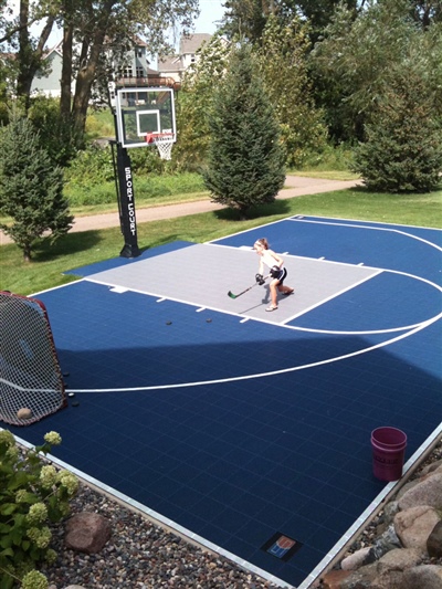 A backyard multi-purpose sports court with a basketball hoop and hockey goal.