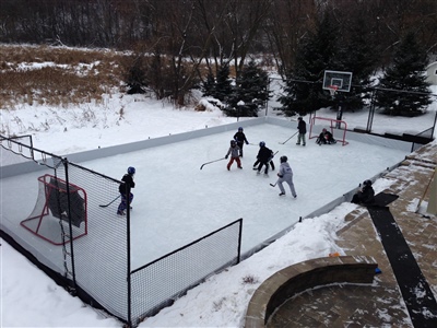 outdoor hockey rink with hockey nets and a basketball hoop with fences on each end. 