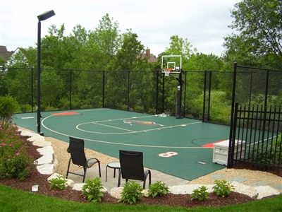 Green basketball court with red key areas painted and multiple logos with a basketball hoop in Sand Creek.