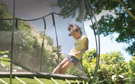 Black trampoline with a black safety net and yellow spring free layer and a child jumping on it.