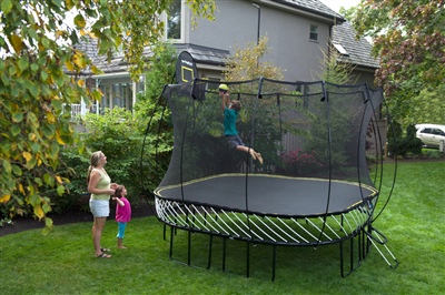 Black trampoline with a black safety net and yellow spring free layer, a child jumping on it, and a basketball hoop.