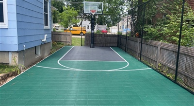 Outdoor residential basketball court with a blue playing surface, surrounded by trees.