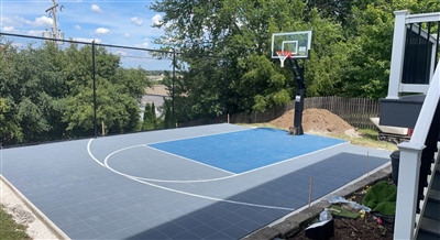 Outdoor basketball court with a white backboard, hoop, and rebounder, surrounded by trees and a clear blue sky in Edina Mn. 