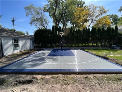 A basketball court with a grey surface and navy blue lines, featuring a sport court logo in the center.