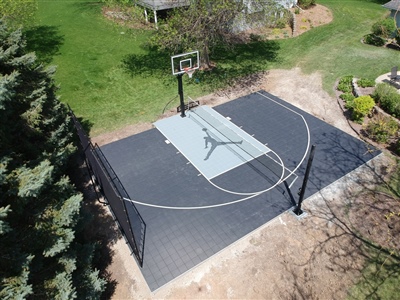 A basketball court with a black and grey surface, featuring white lines and a sport court logo at the center.