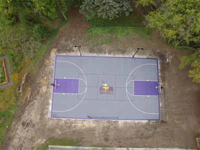 A basketball court with a purple and yellow Vikings-themed surface, featuring white lines and a sport court logo of the Vikings in the center in Chanhassen.