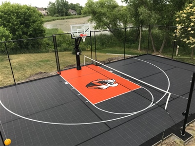 A basketball court with an orange and black surface, white lines, and a sport court logo in the center in Eagan.