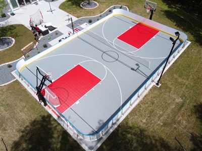 A double sided basketball court with a grey and red surface and white lines with a volleyball net running through it. 