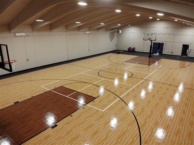 An indoor basketball court with a polished wood surface, brown key areas, and black lines, enclosed by an arched ceiling with bright lighting.