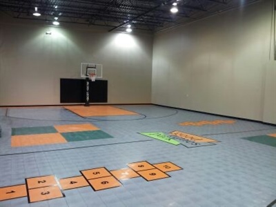  An indoor basketball court with a grey surface, featuring orange and green sections for various sports activities, and a basketball hoop at one end in Apple Valley.