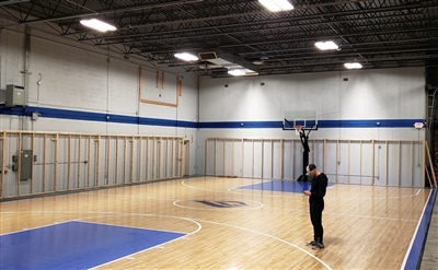 An indoor basketball court with a polished wood surface, blue key areas, black lines, and featuring a central logo in Prior Lake.