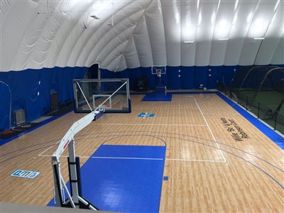 An indoor basketball court with a polished wood surface, blue key areas, and black lines, featuring a white arched ceiling and blue walls in Chaska.