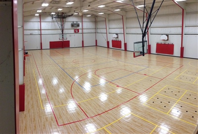 An indoor basketball court with a polished wood surface, red lines, and multiple basketball hoops, featuring a high ceiling with bright lighting.