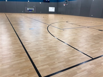 An indoor basketball court with a light wood surface, black lines, and grey walls in Golden Valley.