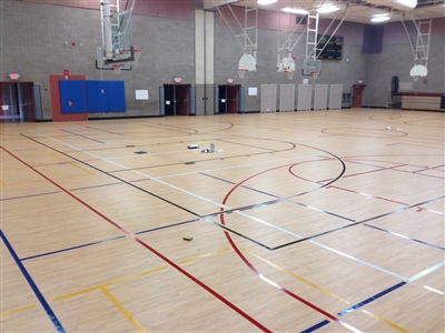 An indoor basketball court with a light wood surface, multi-colored lines, and grey walls, featuring multiple basketball hoops and a central logo in Rosemount.