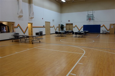 An indoor basketball court with a light wood surface, white lines, and white walls.