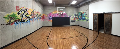 A small indoor basketball court with a polished wood surface, black lines, and black padding behind it.