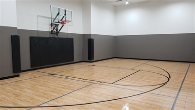 Indoor home basketball court with polished wood flooring, black lines, a basketball hoop, and gray walls with black padding in Credit River.