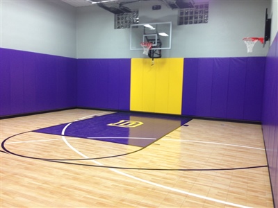 Indoor home basketball court with light wood flooring, purple and yellow wall padding, a purple painted key area, and two basketball hoops in Cottage Grove.