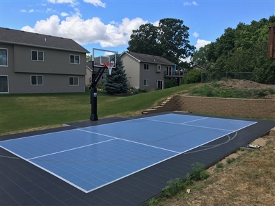 Outdoor residential basketball court with blue and white surface and a black basketball hoop.