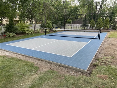 Outdoor residential court with blue and gray surface, featuring a pickleball nets, and surrounded by trees in Douglas.