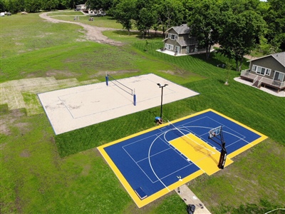 Outdoor residential sports area with a blue and yellow basketball court and a sand volleyball court.