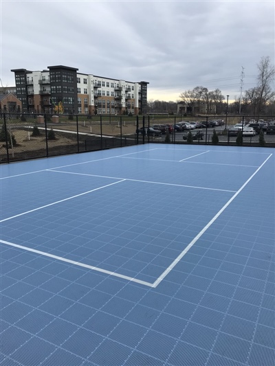 Outdoor sports court with a blue surface and white lines, surrounded by a black fence.