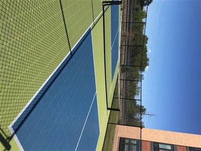 Outdoor sports court with a green and blue surface, white lines, and a black fence.