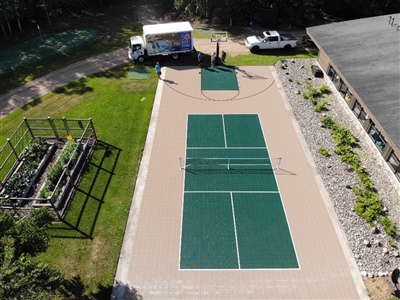 Outdoor residential sports court with a beige and green surface and a tennis court. 