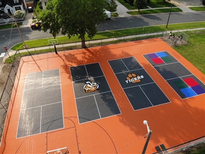  Outdoor sports court with an orange surface, black and gray play areas, colorful sections, and a basketball hoop.