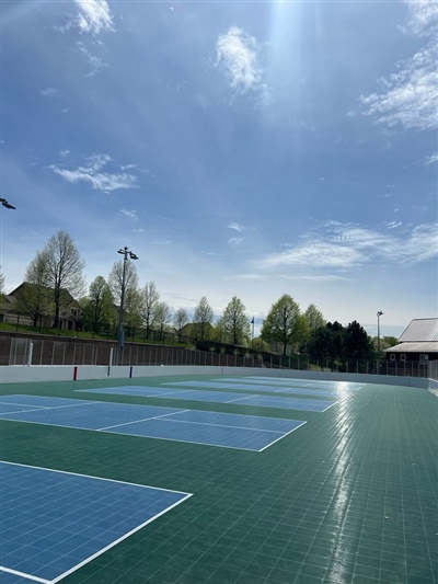 Multiple outdoor sports courts with a green surface and blue and white tennis courts. 