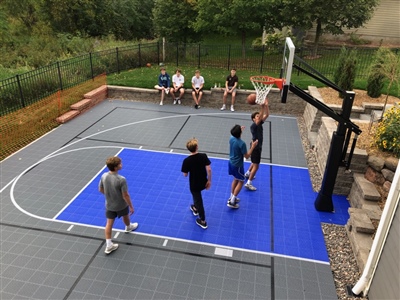 Outdoor residential basketball court with a gray and blue surface with white and black lines.